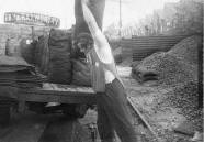 A coalman at a coal yard loading sacks of coal onto a delivery lorry, mid 20th century